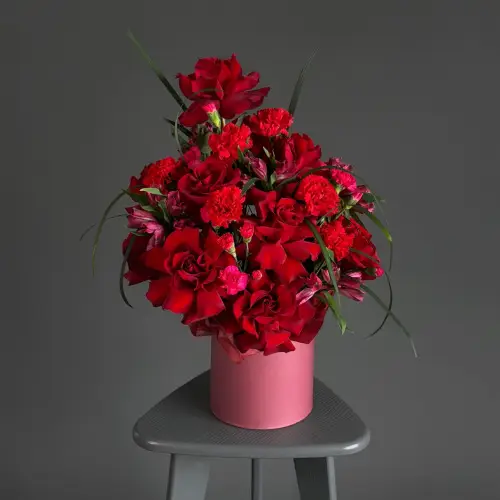 Цветочная композиция из красных гвоздик и роз с берграссом в шляпной коробке